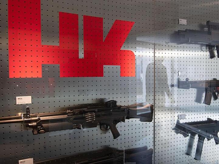 Das Logo des Waffenherstellers Heckler & Koch ist auf dem Firmengelände an einer Präsentationswand neben Waffen zu sehen.
