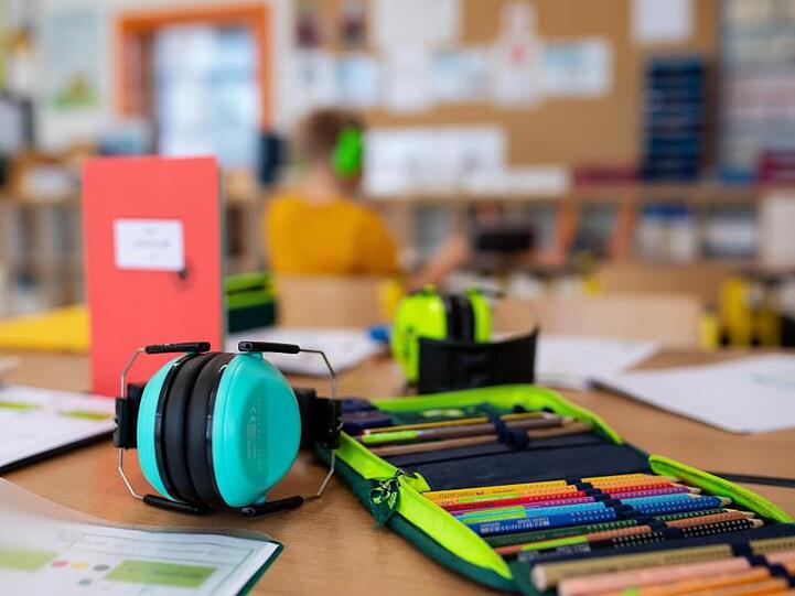 Ein Mäppchen und ein Gehörschutz liegen im Klassenzimmer einer Grundschule auf einem Tisch. (Archivbild)