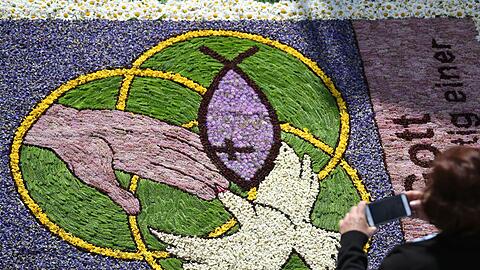Eine Frau fotografiert an Fronleichnam während der Prozession Kirchenmotive in einem Blumenteppich.