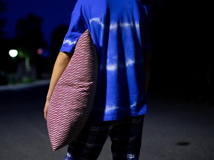 Ein Junge im Schlafanzug steht nachts mit einem Kissen in der Hand auf einer Straße. Foto: Sven Hoppe