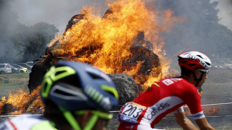 13. Juli 2018: Teilnehmer der Tour de France fahren an einem brennenden Heuhaufen in der Bretagne vorbei.