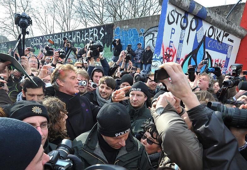 Der amerikanische Schauspieler und Sänger David Hasselhoff geht umringt von Demonstranten und Polizisten zur East Side Gallery, einem künstlerisch gestalteten Restabschnitt der früheren Berliner Mauer.