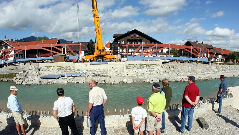 ARCHIV - Passanten beobachten am 05.09.2006 in der oberbayerischen Ortschaft Eschenlohe im Landkreis Garmisch-Partenkirchen am Ufer des Fluss Loisach den Bau von Hochwasserschutzdeichen und einer Brücke. ARCHIV - Passanten beobachten am 05.09.2006 in der oberbayerischen Ortschaft Eschenlohe im Landkreis Garmisch-Partenkirchen am Ufer des Fluss Loisach den Bau von Hochwasserschutzdeichen und einer Brücke.