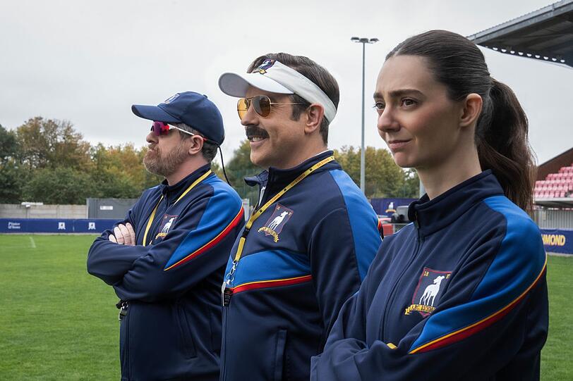 Mit Coach Beard (Brendan Hunt) und der schroffen Alice Chilton (Tanya Reynolds) hat Ted Lasso (Jason Sudeikis, Mitte) zwei hervorragende Co-Trainer an seiner Seite.
