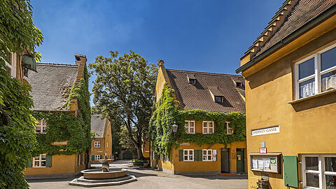 Idylle mitten in der Großstadt Augsburg: Ockerfarbige Häuser bestimmen das Bild der Fuggerei, deren Zentrum ein schlichter Brunnen bildet.