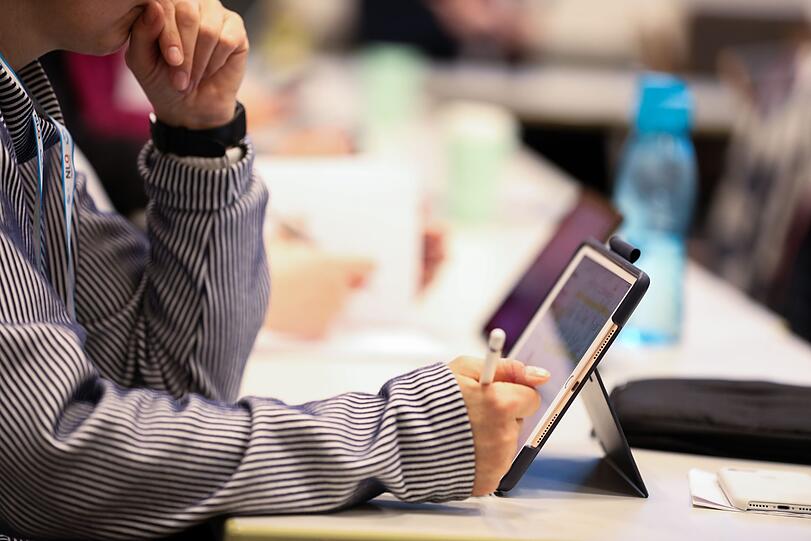 Eine Frau sitzt während der bundesweiten Lehrerfortbildung zur Digitalisierung im Klassenzimmer bei einem Workshop an einem Tisch und hat einen Tabletcomputer vor sich stehen.