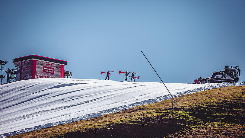 Bei strahlendem Sonnenschein ziehen sich weiße Kunstschnee-Teppiche durch die Kitzbüheler Alpen - befremdliche Bilder von der Saisoneröffnung.