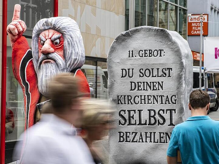 Die Innenstadt Dortmunds steht ganz im Zeichen Kirchentags. In einer Fußgängerzone ist eine Moses-Pappfigur platziert - auf der "11. Gebot: Du sollst deinen Kirchentag selbst bezahlen" steht.