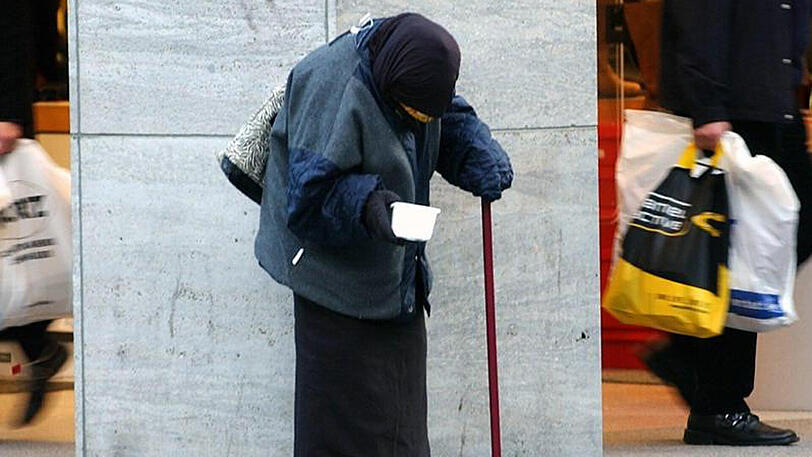 In der Kölner Innenstadt bittet eine alte Frau um Almosen.
