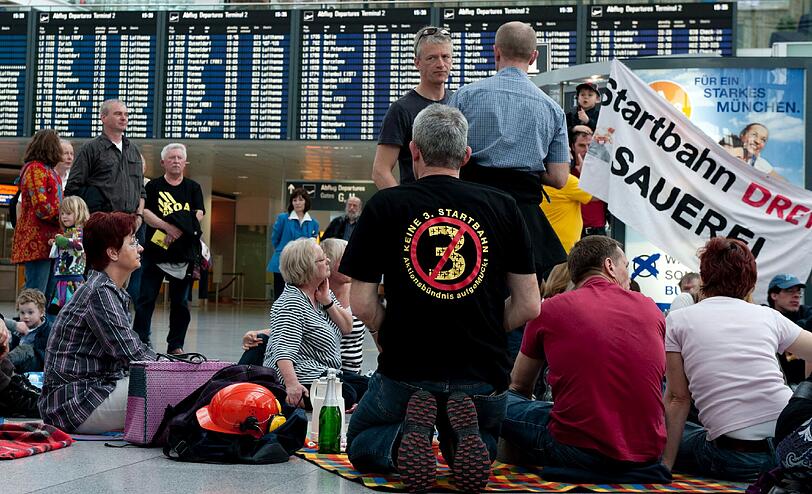 Demonstranten sitzen am Samstag (24.03.2012) am Terminal 2 des Münchner Flughafens auf Picknickdecken. Der Bund Naturschutz und das Aktionsbündnis AufgeMUCkt haben zum Protest-Picknick aufgerufen, um gegen den Bau einer dritten Startbahn am Münchner Flughafen zu demonstrieren.