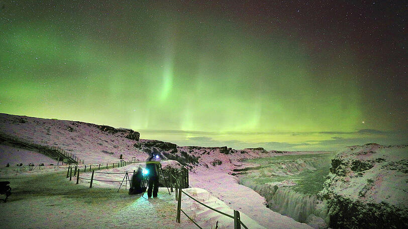 Polarlichter lassen am Gullfoss Wasserfall (Island) den Nachthimmel in grünem Licht erstrahlen.