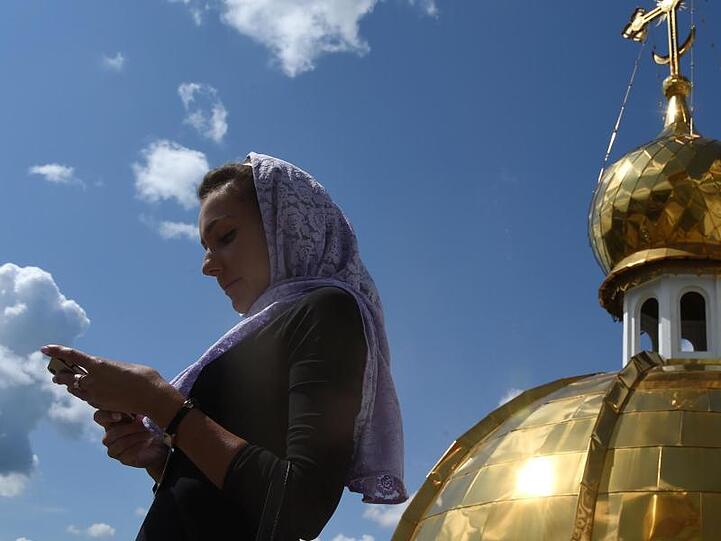 Eine Frau schaut auf dem Dach der orthodoxen Kathedrale von St. Theodor Uschakow in Saransk, Russland, auf ihr Smartphone.