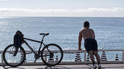 Ein Mann mit nacktem Oberkörper macht am Strand von Nizza neben seinem Fahrrad Übungen. (Archivbild)