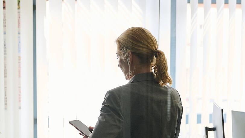 Eine Frau steht in einem Bürozimmer und hält ein Smartphone in der Hand (gestellte Szene).