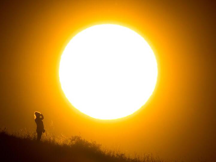 Eine Spaziergängerin steht vor der untergehenden Sonne. Foto: Julian Stratenschulte/Archiv