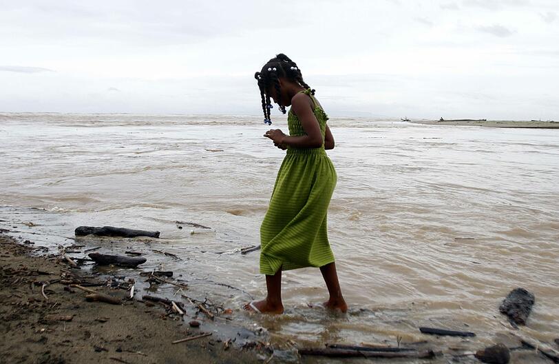 Ein Mädchen läuft am Strand von Hispaniola (Haiti/Dominikanische Republik) durch den starken Regen. Um sie herum: Verwüstung.