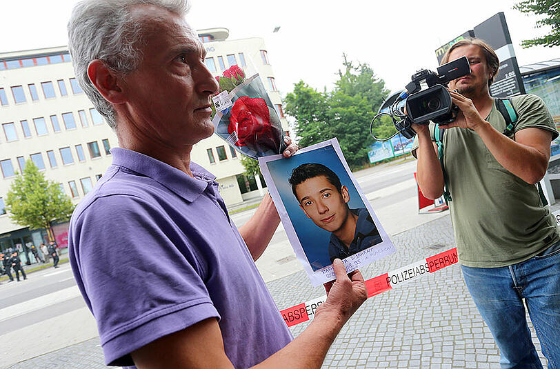 Naim Zabergja steht mit einem Foto seines getöteten Sohnes Dijamant vor dem Olympia-Einkaufszentrum.