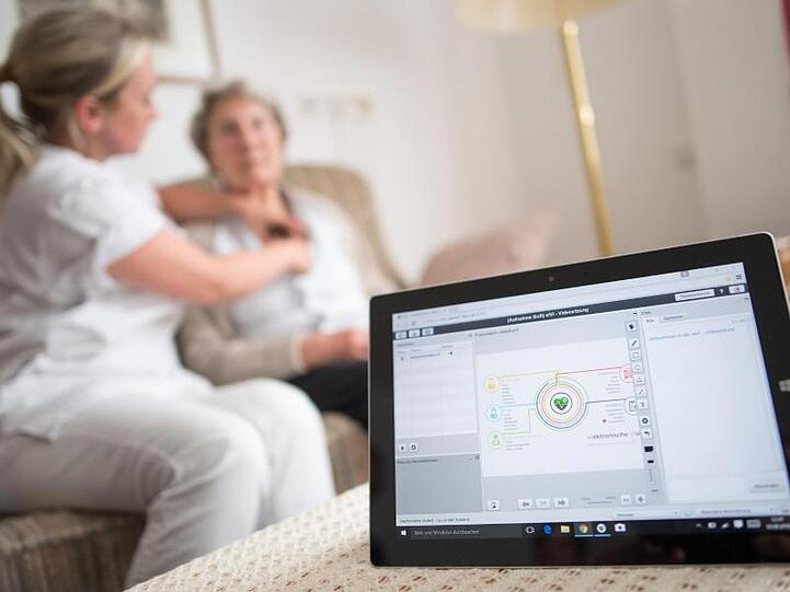 Eine Pflegerin legt einer Bewohnerin im Rahmen einer elektronischen Visite ein EKG-Gerät an, dass die Daten an einen Tablet-Computer und von dort aus zum Arzt überträgt.