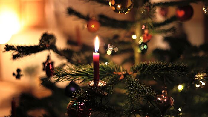 Eine Kerze brennt an einem festlich geschmückten Weihnachtsbaum.