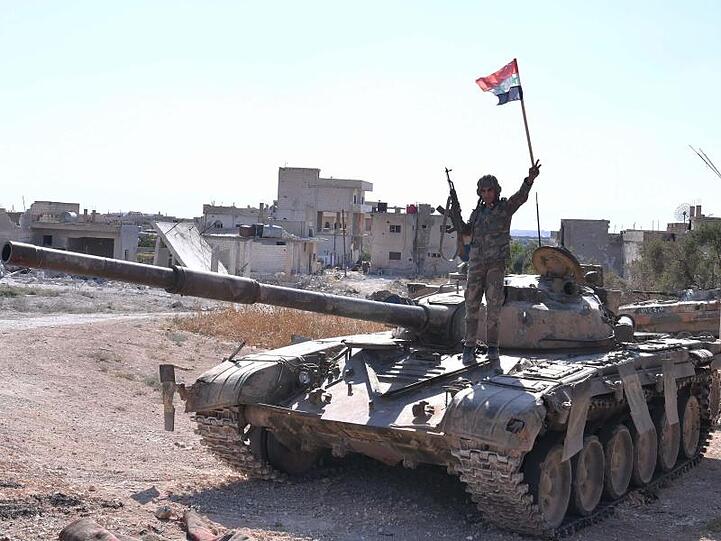 Ein syrischer Soldat zeigt auf einem Panzer das Victory-Zeichen.