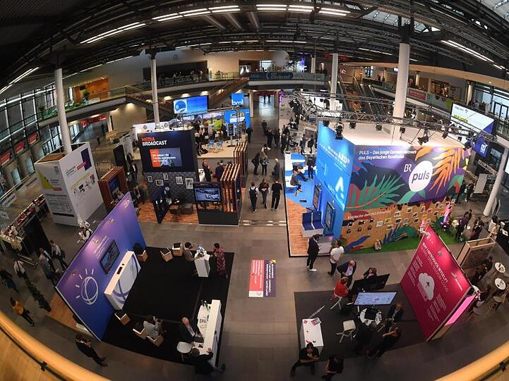 Besucher gehen am ersten Tag der 33. Medientage München in der Messe München durch die Haupthalle. Foto: Felix Hörhager/dpa