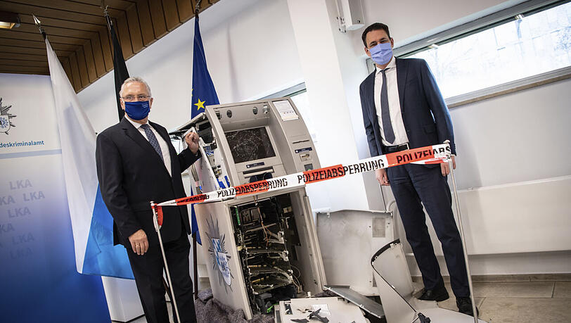 Innenminister Joachim Herrmann (CSU) und Justizminister Georg Eisenreich (CSU) stehen zur Vorstellung  des Lagebilds der Organisierten Kriminalität beim Landeskriminalamt neben einem gesprengten Geldautomaten.