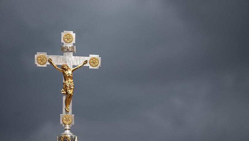 Ein katholisches Kruzifix ist vor dunklen Wolken zu sehen.
