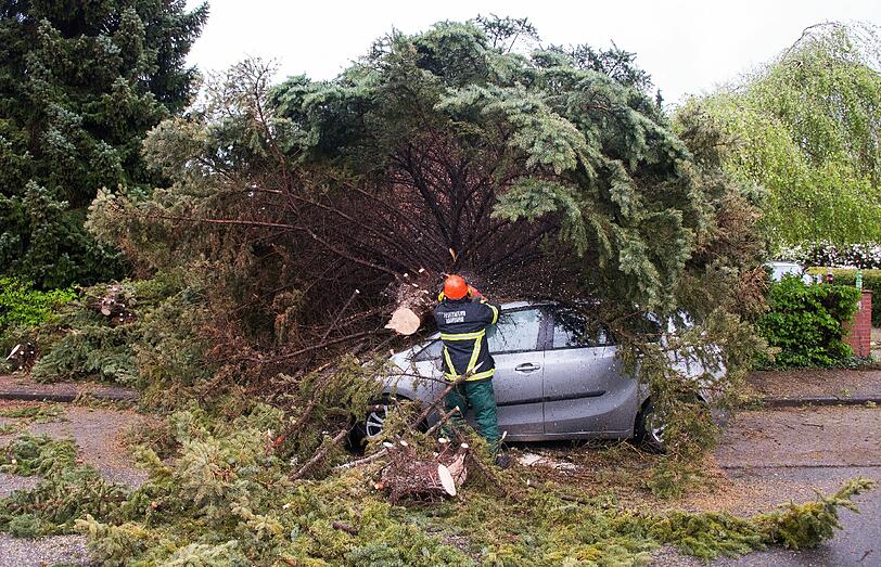 Ein Feuerwehrmann zersägt in Hamburg-Rahlstedt einen auf ein Auto gestürzten Baum.