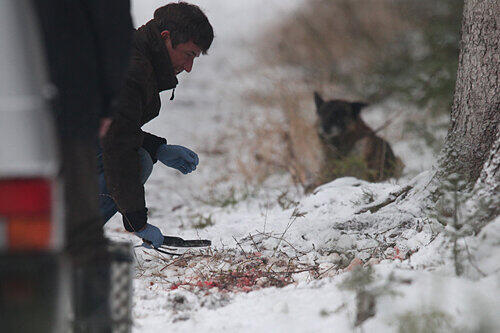 Mit einem Metalldetektor wird nach der Tatwaffe im blutigen Schnee gesucht.