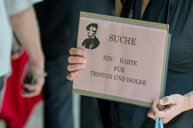 Eine Frau hält vor der Eröffnung der 104. Bayreuther Festspiele in Bayreuth vor dem Festspielhaus ein Schild mit der Aufschrift "Suche eine Karte für Tristan und Isolde".