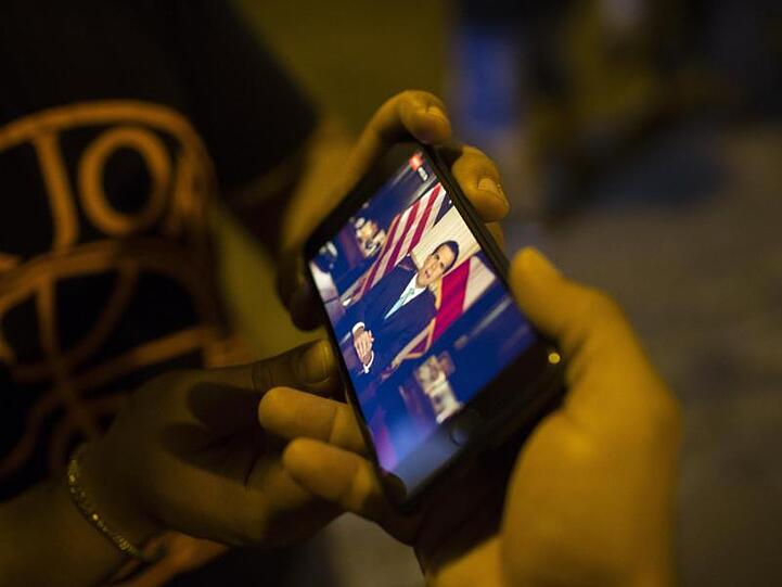 Puerto-Ricaner verfolgen auf einem Smartphone eine Videoaufzeichnung, in der Gouverneur Rosselló seinen Rücktritt zum 2. August ankündigt.