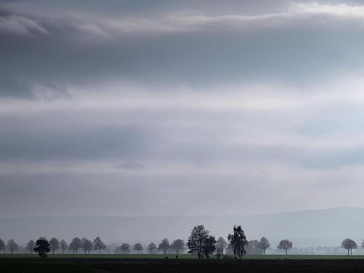 Trübes Wetter und dichte Wolken ziehen über eine ländliche Landschaft. Foto: Peter Steffen/Archivbild