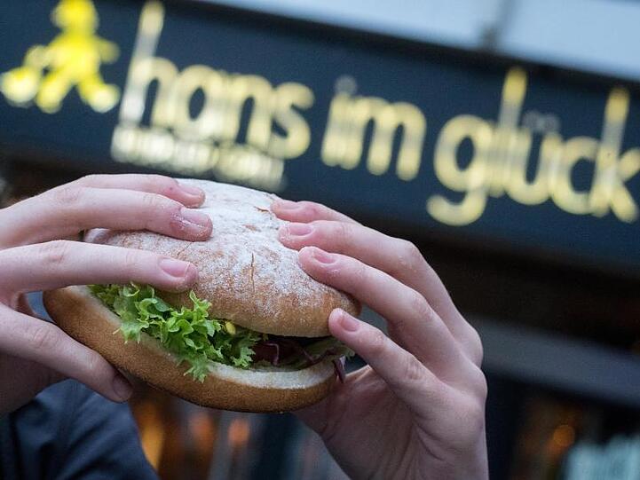 Eine junge Frau hält einen Burger der Burger-Kette "Hans im Glück" in den Händen. Foto: Matthias Balk/dpa/Archivbild