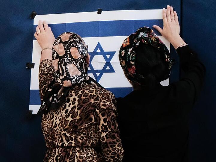 Zwei Mitarbeiterinnen des Wahlausschusses befestigen in einem Wahllokal in Jerusalem eine israelische Fahne.