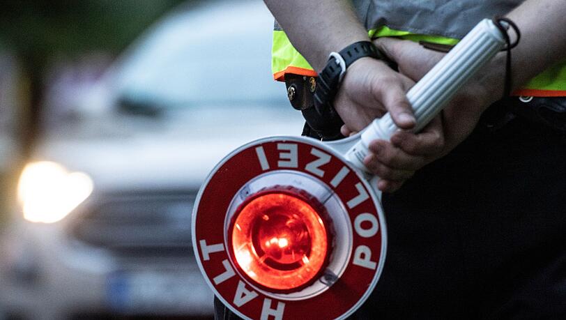 Ein Polizist hält an einer Kontrollstelle eine Winkerkelle in der Hand.