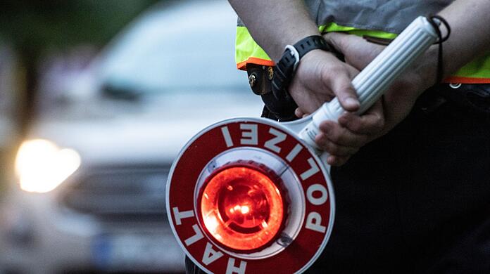 Ein Polizist hält an einer Kontrollstelle eine Winkerkelle in der Hand.