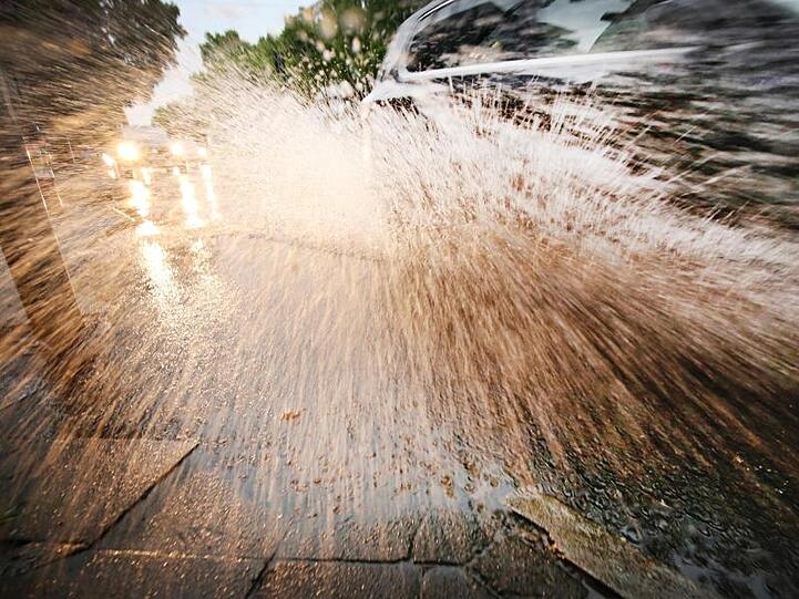 Ein Auto fährt durch eine Wasserlache auf der Straße. Foto: Martin Gerten