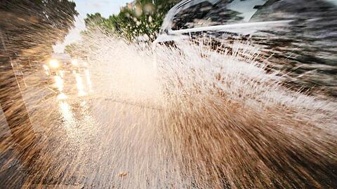 Ein Auto fährt durch eine Wasserlache auf der Straße. Foto: Martin Gerten