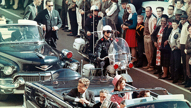 Präsident John F. Kennedy und Gattin Jackie Kennedy lächeln den Menschen am Straßenrand zu. Nur wenige Minuten später, als die Autokolonne die Dealey Plaza erreicht, fallen die tödlichen Schüsse. Präsident John F. Kennedy und Gattin Jackie Kennedy lächeln den Menschen am Straßenrand zu. Nur wenige Minuten später, als die Autokolonne die Dealey Plaza erreicht, fallen die tödlichen Schüsse.