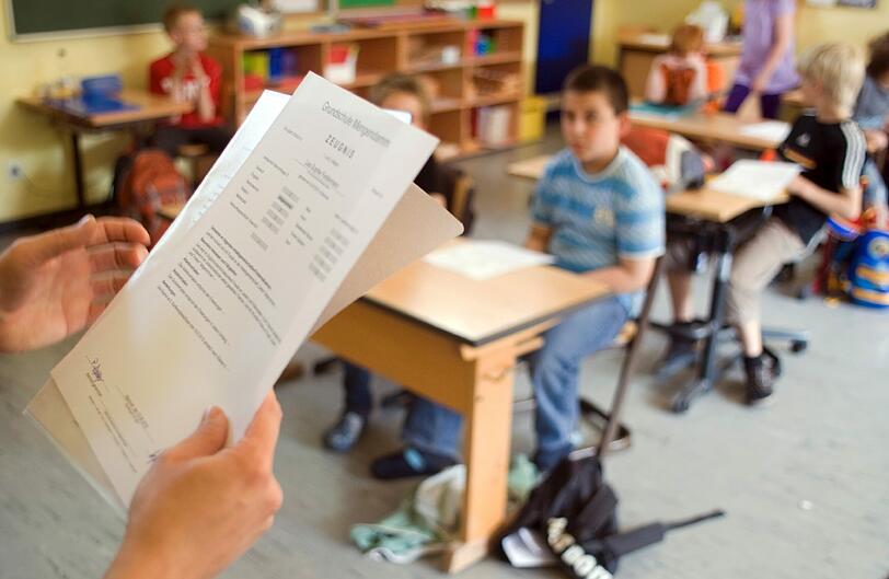 Eine Lehrerin verteilt klassische Zeugnisse: Doch in einem Viertel der Münchner Grundschulen nehmen Schüler am Freitag eine neue Art Zeugnis mit in die Faschingsferien.