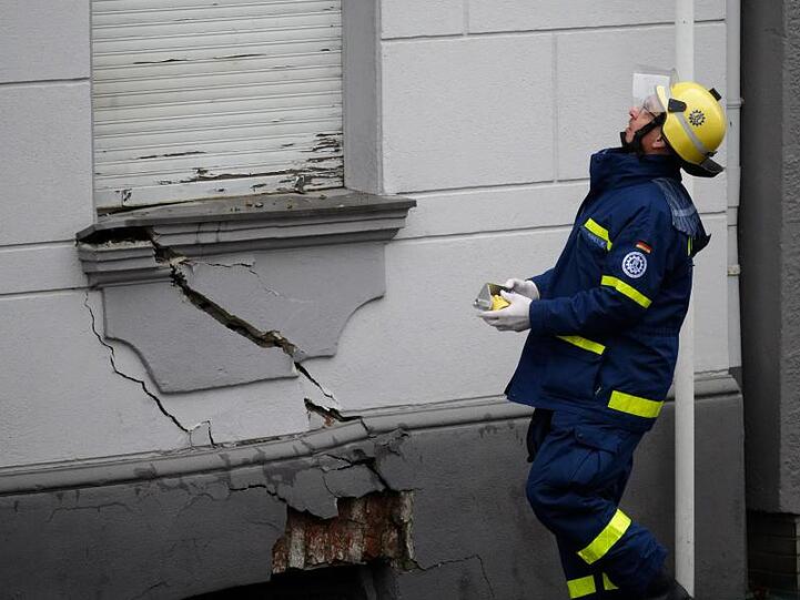 Ein Mitarbeiter des Technischen Hilfswerks steht in Wuppertal vor einem der Häuser, an dem ein breiter Riss sichtbar ist.