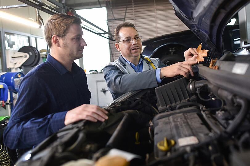 Ein Mechaniker geht mit einem Kunden die Probleme im Motorraum durch.