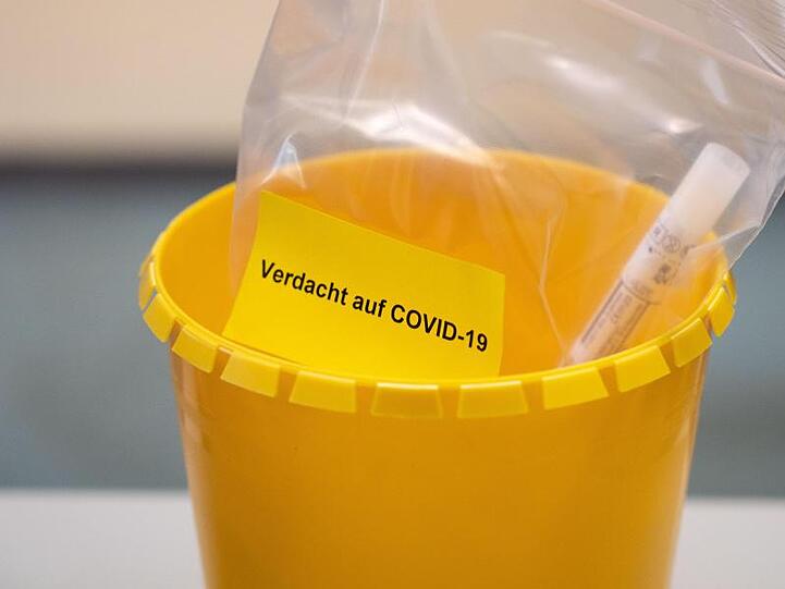 Ein Teströhrchen liegt in einer Tüte mit der Aufschrift "Verdacht auf COVID-19".