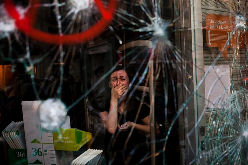 Mireia Arnau (39) sieht durch die zerbrochene Scheibe ihres Ladens in Barcelona, nachdem Demonstranten mit der Polizei während des Generalstreiks am 29. März zusammengestoßen waren. Der Streik war gegen die Arbeitsmarktreform der Regierung ausgerufen worden. In einem Klima anhaltender wirtschaftlicher Probleme hatte das Parlament einschneidende Kürzungen vorgeschlagen, sowie Maßnahmen, die den Firmen die Entlassung von Mitarbeitern erleichterten. Spaniens Arbeitslosigkeit war auf über 24 Prozent gestiegen, der höchste Prozentsatz in der EU. Die Hälfte der unter 25-Jährigen war ohne Arbeit. Die meisten Proteste im Land verliefen friedlich, nur in Barcelona warfen einige Demonstranten Steine auf Bankgebäude und Geschäfte.