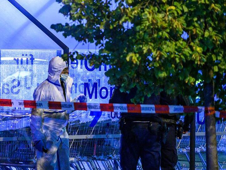Einsatzkräfte der Polizei stehen auf einem Parkplatz neben einem Supermarkt, vor dem Schüsse gefallen sind. Foto: Armin Weigel/dpa