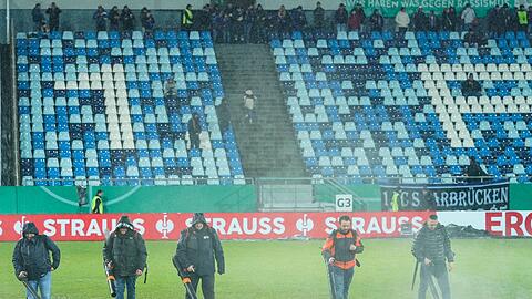Im Ludwigspark-Stadion versuchen Helfer, Wasserlachen vom Spielfeld zu entfernen.