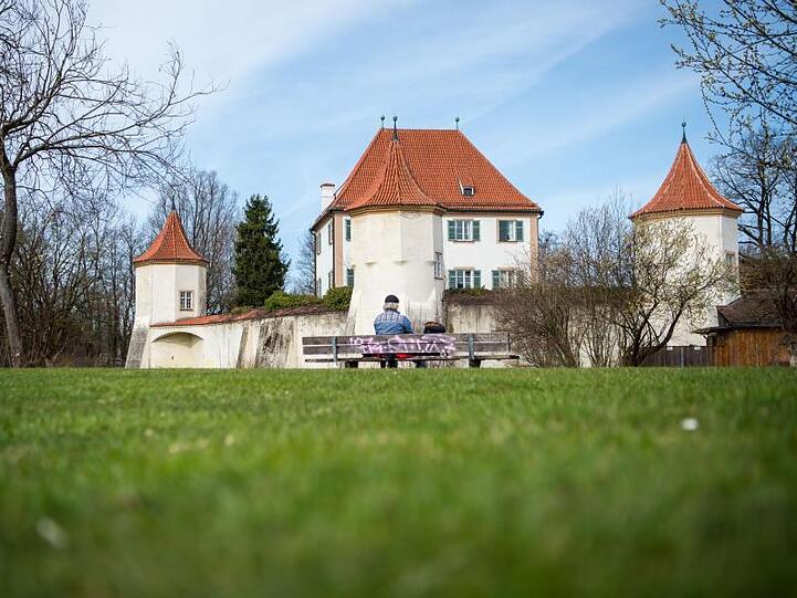 Ein Mann sitzt bei sonnigem Wetter vor dem Schloss Blutenburg. Foto: Lino Mirgeler/dpa/Symbolbild