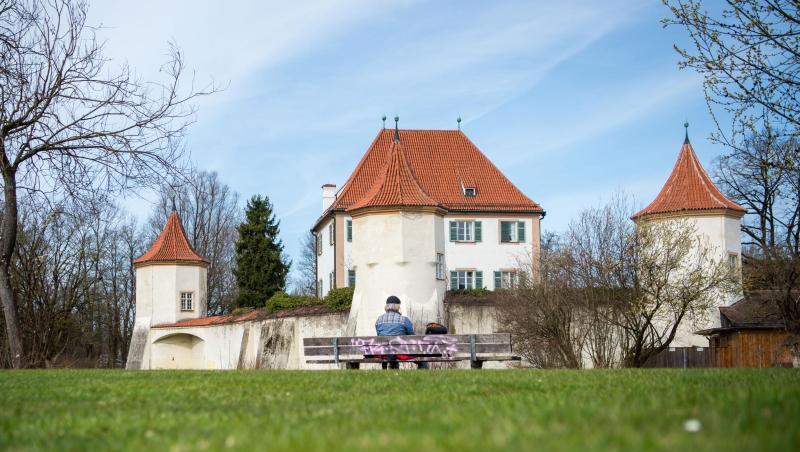 Ein Mann sitzt bei sonnigem Wetter vor dem Schloss Blutenburg. Foto: Lino Mirgeler/dpa/Symbolbild