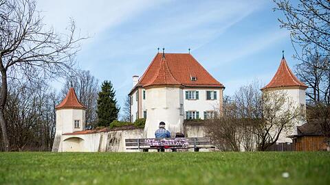 Ein Mann sitzt bei sonnigem Wetter vor dem Schloss Blutenburg. Foto: Lino Mirgeler/dpa/Symbolbild