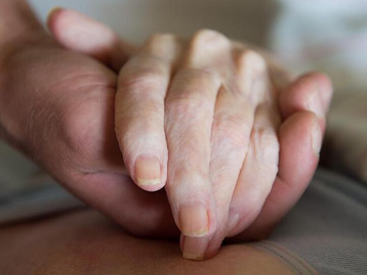 Ein Altenpfleger hält in einem Pflegeheim die Hand einer Frau.